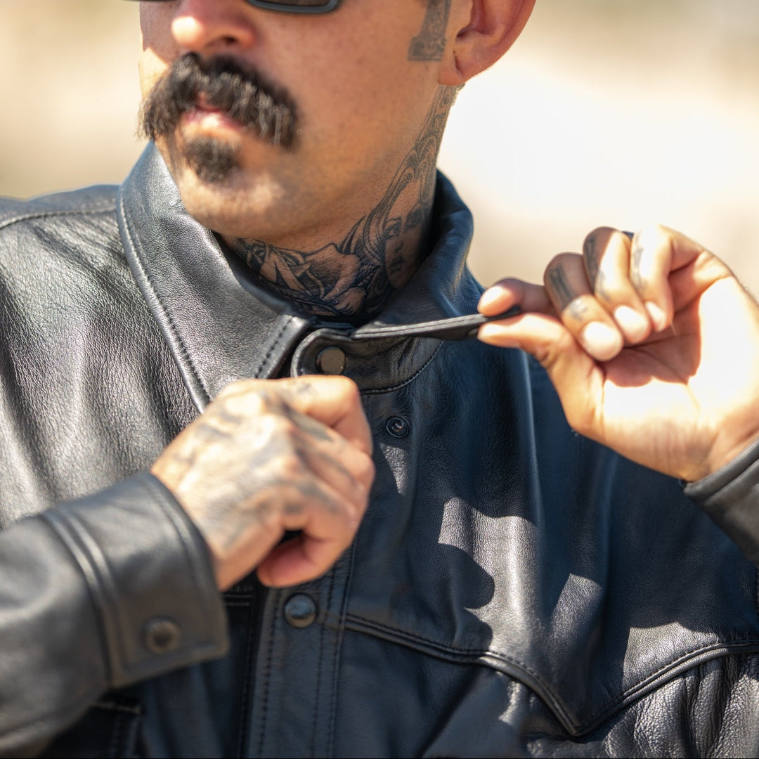 Man wearing a camouflage 'Dodgers' cap and sunglasses, holding a small object.