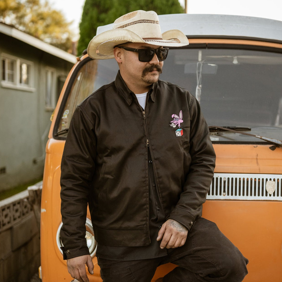 Man wearing a cowboy hat and sunglasses standing next to an orange van.