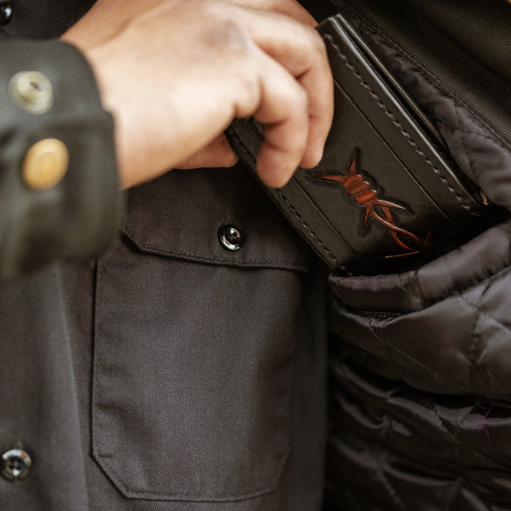 Person opening a dark brown leather wallet with a logo on a dark jacket.