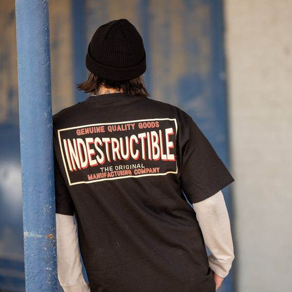 Person wearing a black 'Indestructible' t-shirt with text on the back, standing against a blue wall.